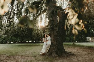 Someone standing beside a large oak tree in a park setting during golden hour sunlight.