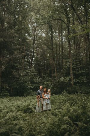 Family group posed among lush green ferns in a wooded forest setting during a summer photoshoot.