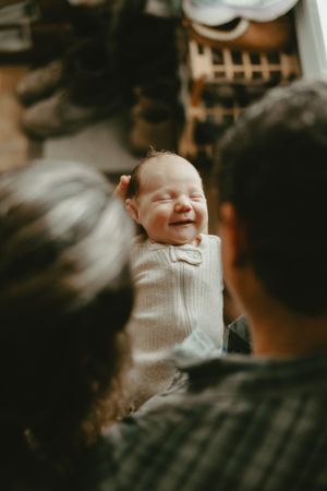 A newborn baby in white clothing smiles joyfully while being held in a dimly lit setting.