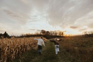 Two silhouettes run through a golden cornfield at sunset creating a dreamy autumn scene.