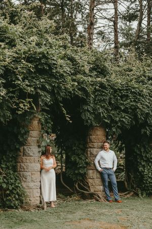 Two figures stand in stone archways covered with lush green ivy in a garden setting.