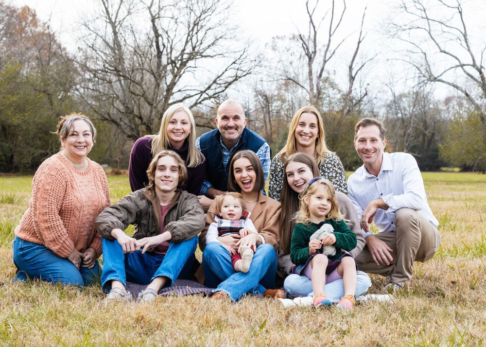 Multi-generational group gathered outdoors on grass for a casual family photo shoot.