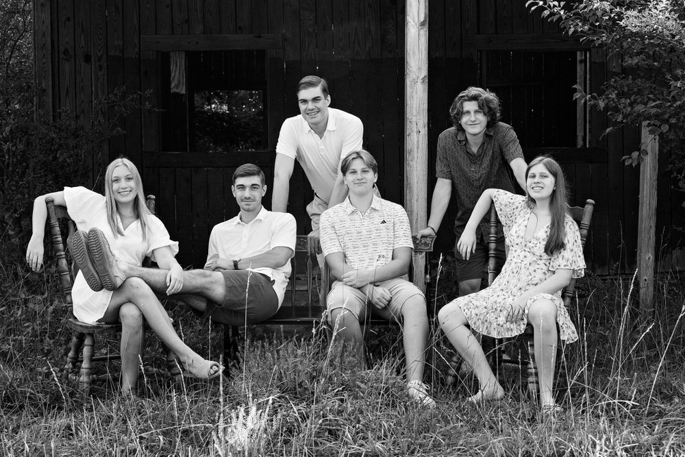 Black and white portrait of five people sitting casually outdoors near a dark building.