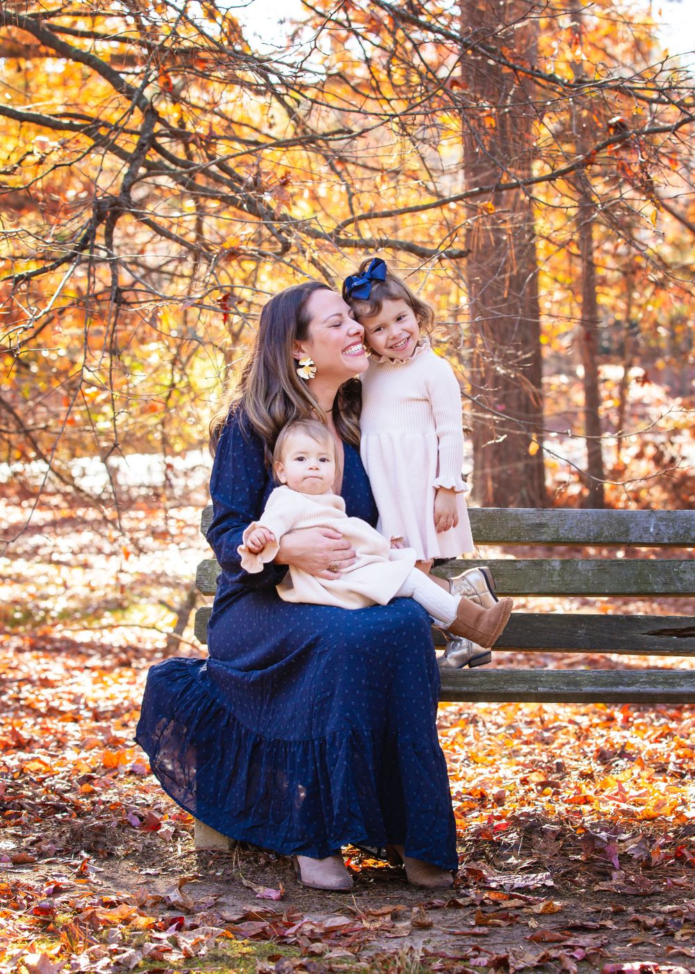 Family portrait on wooden bench surrounded by golden autumn trees.