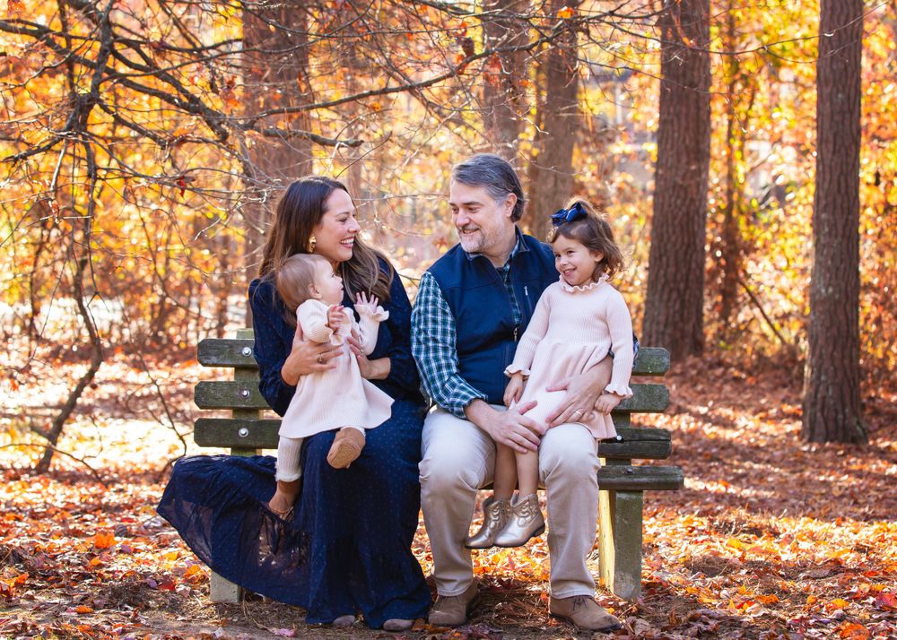 Family seated on wooden bench during fall photo session in wooded setting.