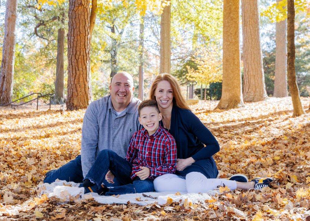 Family sitting together on white blanket surrounded by fall foliage.