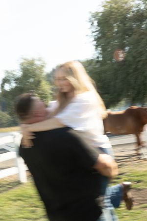 A couple embraces joyfully outdoors near a horse pasture, captured in a dreamy motion blur effect.