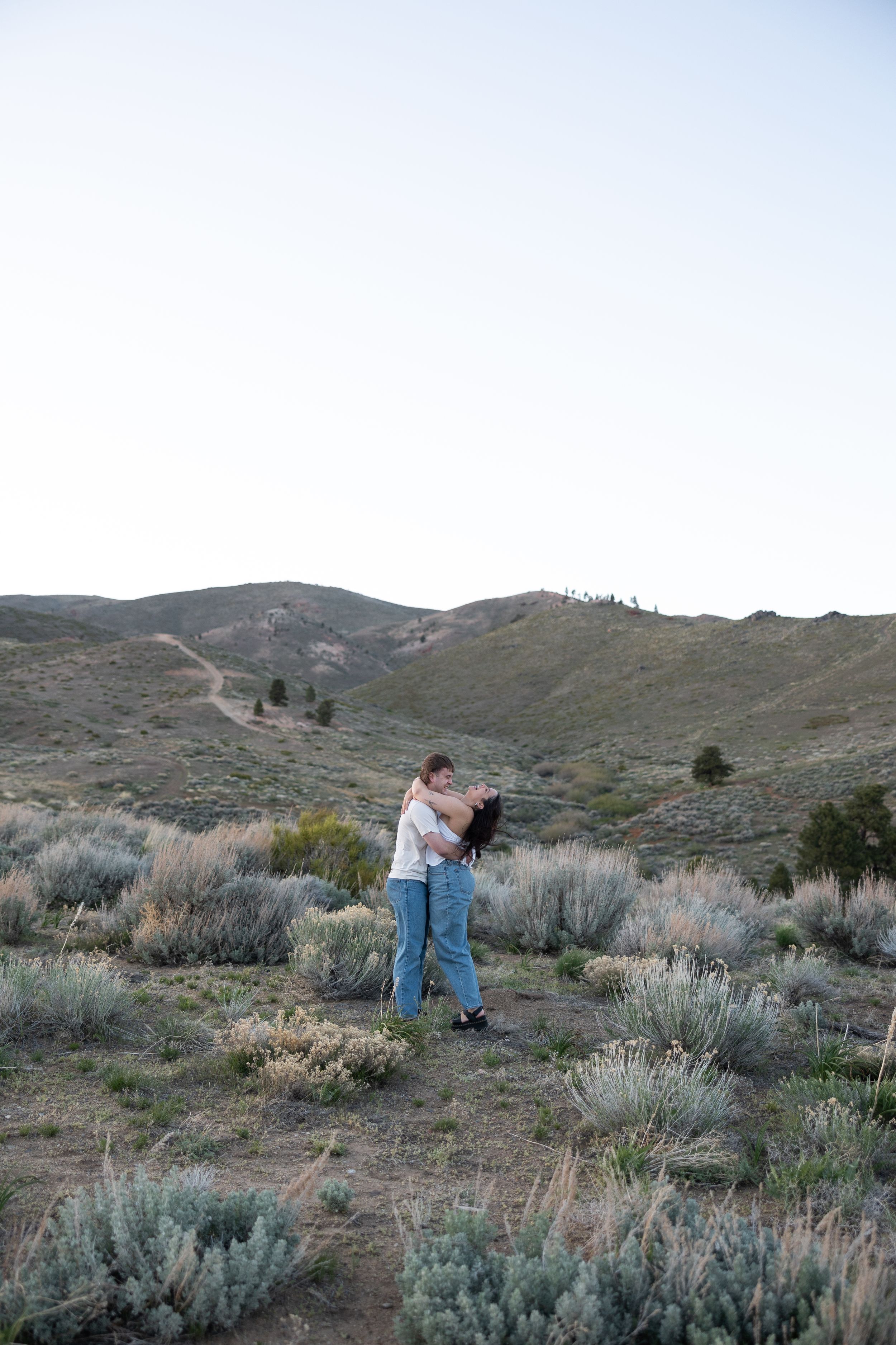 Couple dancing and embracing in vast sagebrush desert landscape at dusk.