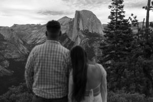 Black and white photo of couple viewing Half Dome at Yosemite National Park from scenic overlook at dusk.