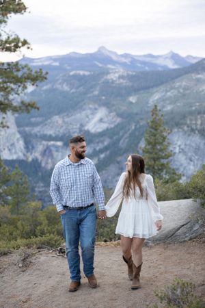 Couple holding hands on a mountain trail with stunning Yosemite valley views in the background.
