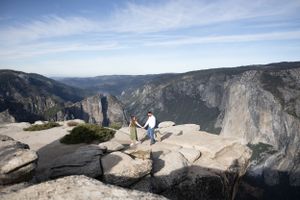 Couple standing on granite rock overlooking vast Yosemite valley canyon landscape.