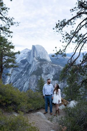 Couple gazing at each other on a forest trail with iconic Half Dome in background.
