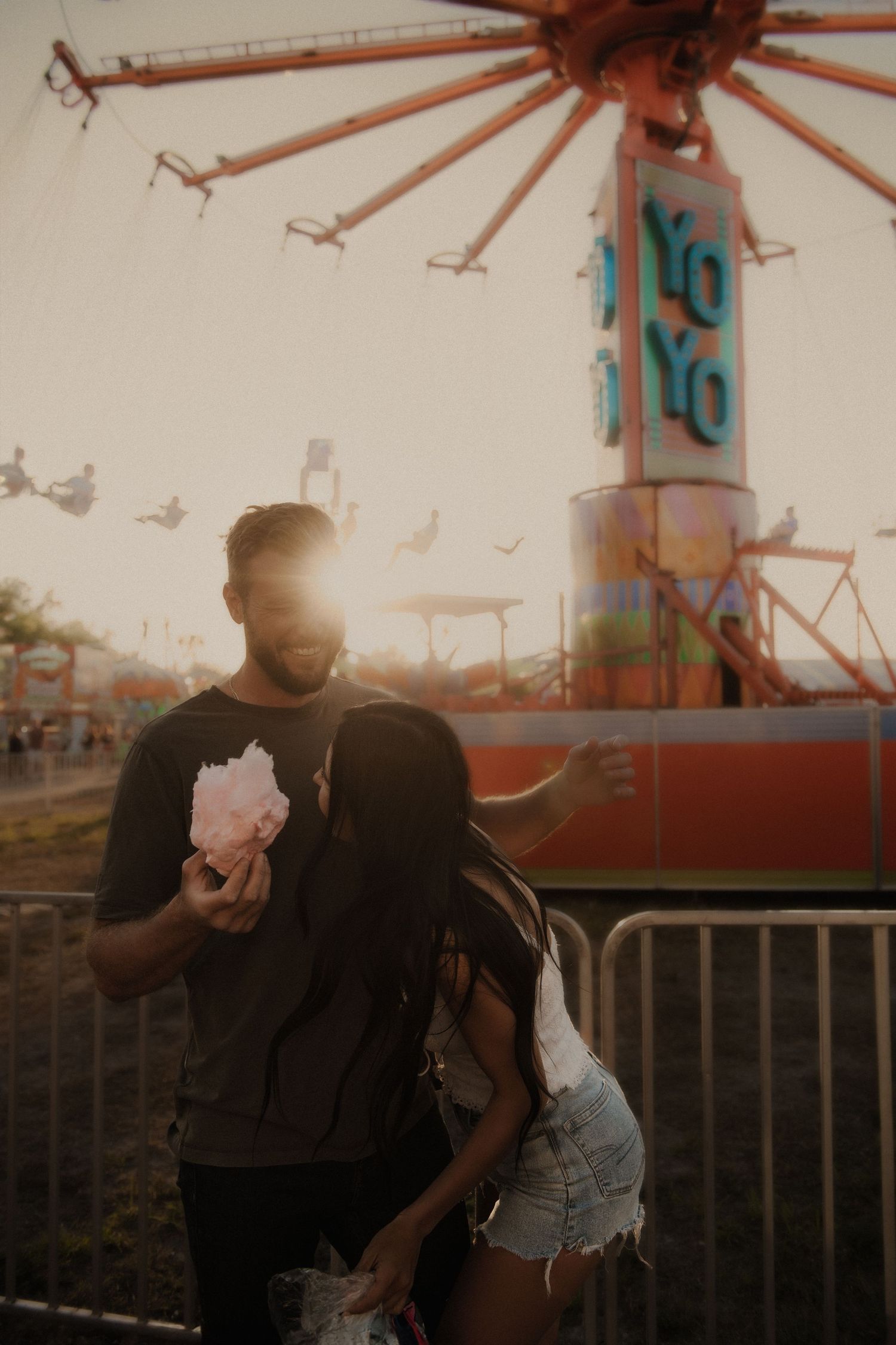 Couple sharing a romantic moment at a carnival with a Yo-Yo ride in the background.