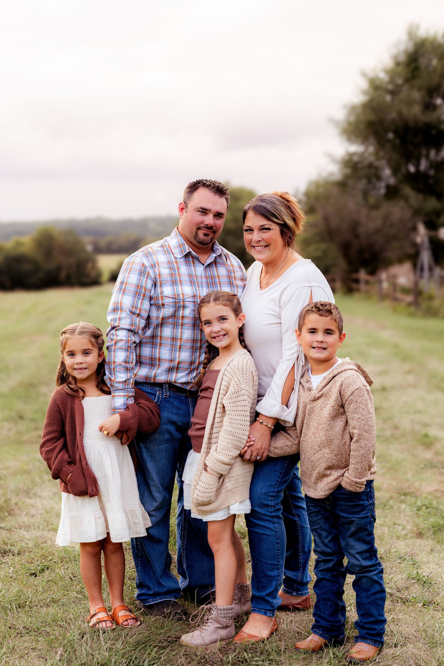 Family portrait in a rustic field during golden hour wearing coordinated neutral outfits.