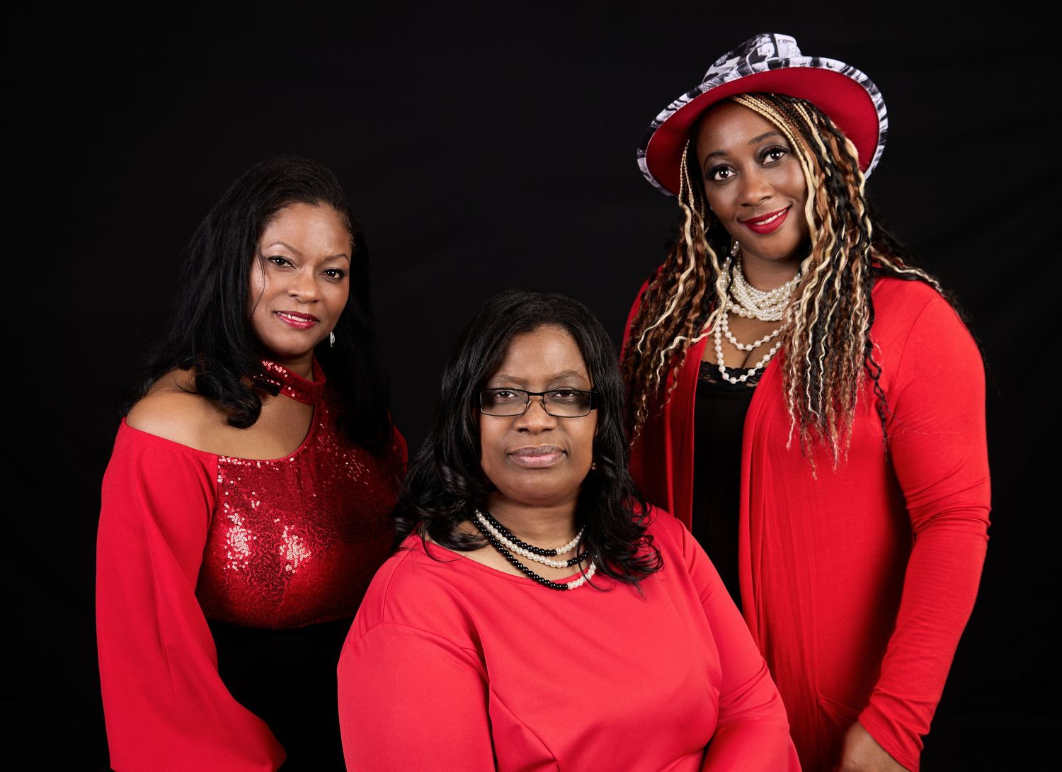 Group portrait of people wearing matching red outfits against dark studio background.