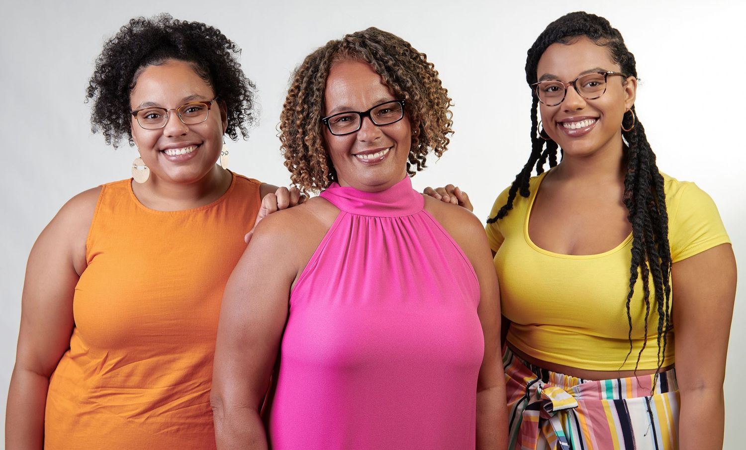 Group portrait of people wearing bright orange, pink and yellow tops against white background.