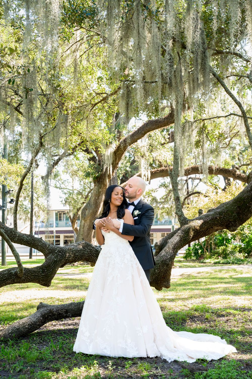 A couple in wedding attire shares romantic moments under majestic oak trees draped with Spanish moss.
