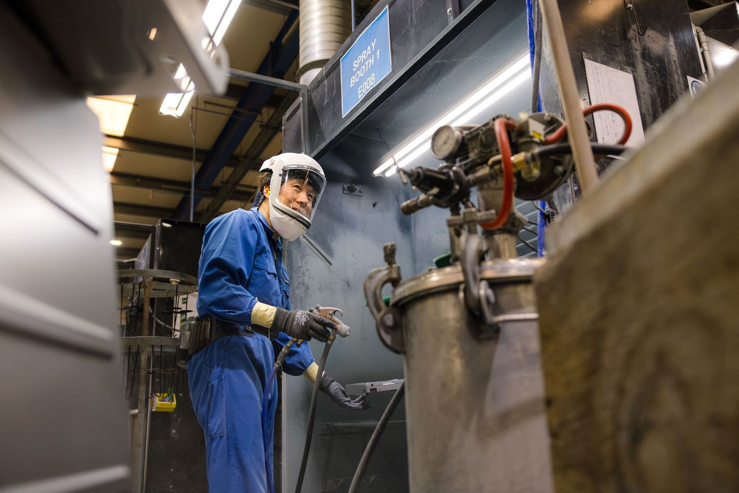 Industrial worker in blue coveralls and protective helmet operating machinery in a manufacturing facility.