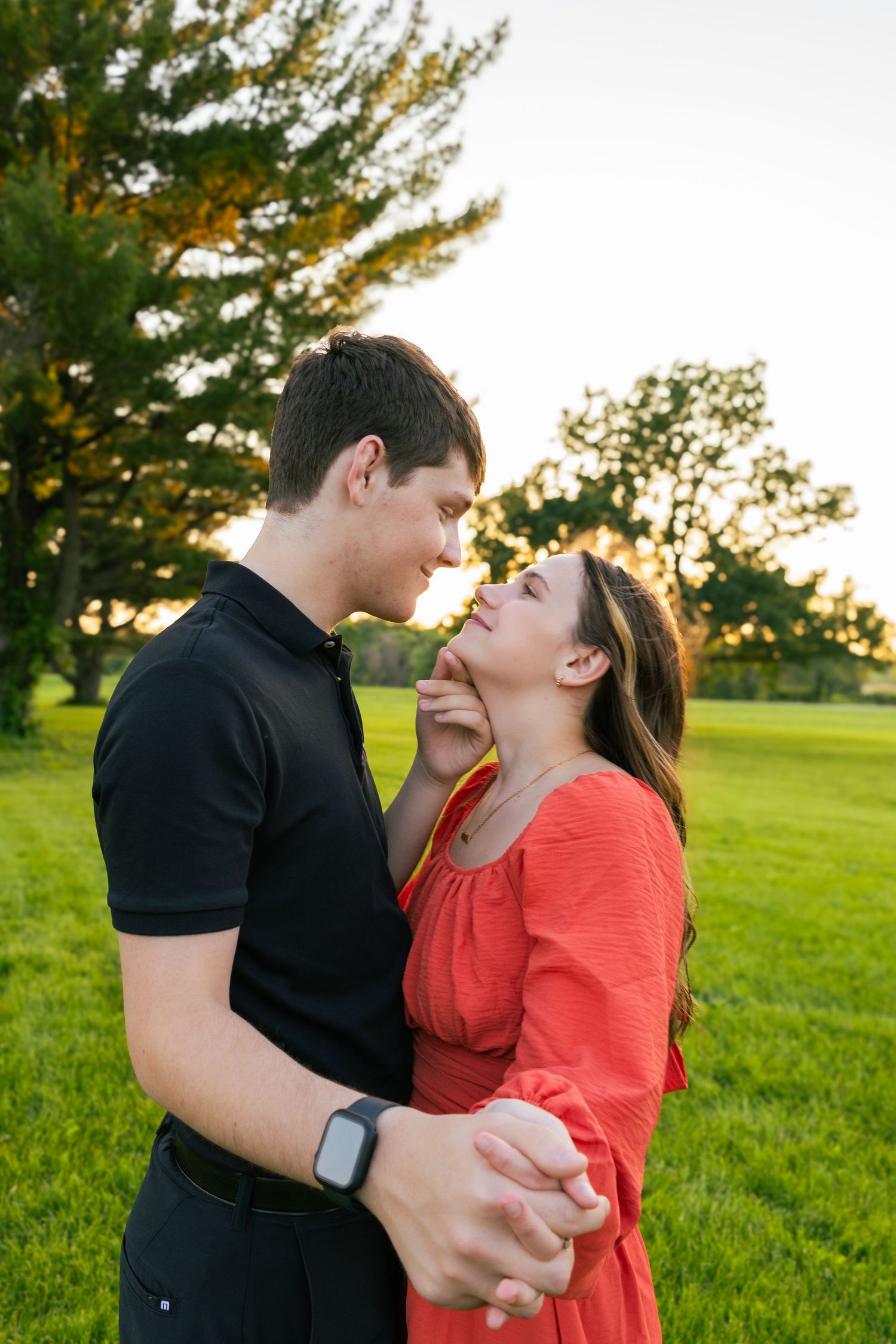 Couple in black and coral outfits sharing intimate moment in park at sunset.