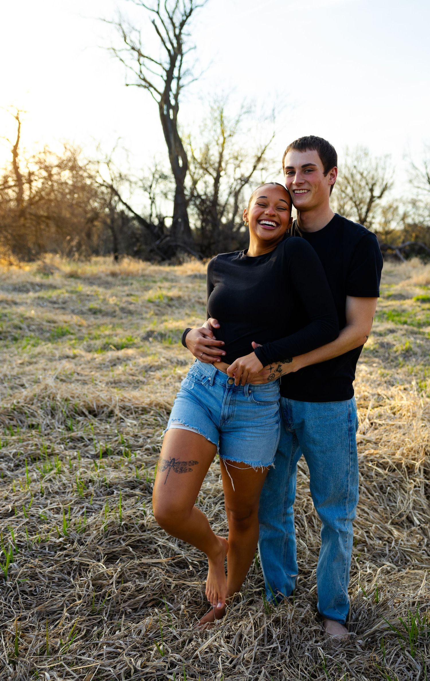 A romantic outdoor photoshoot of a couple wearing casual outfits in a natural setting at golden hour.