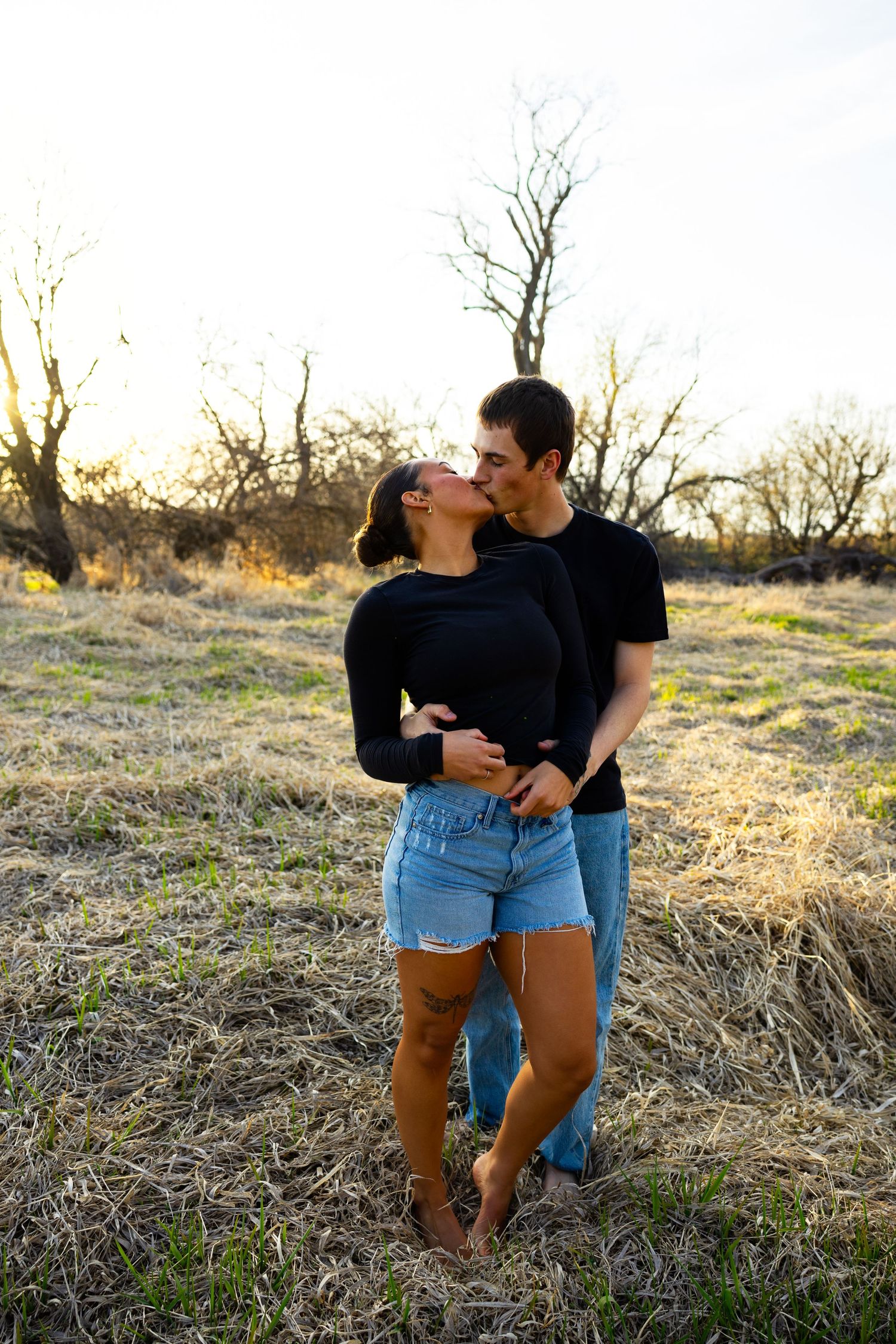 A candid moment between a couple sharing laughter in an outdoor setting with bare trees.