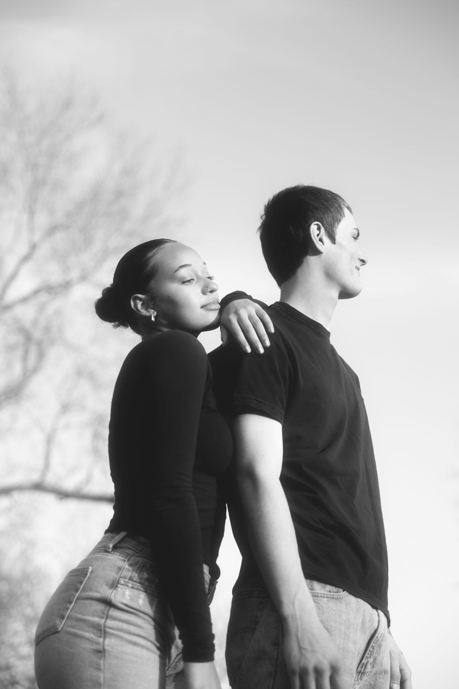 A black and white intimate portrait of two people in casual attire standing close together.