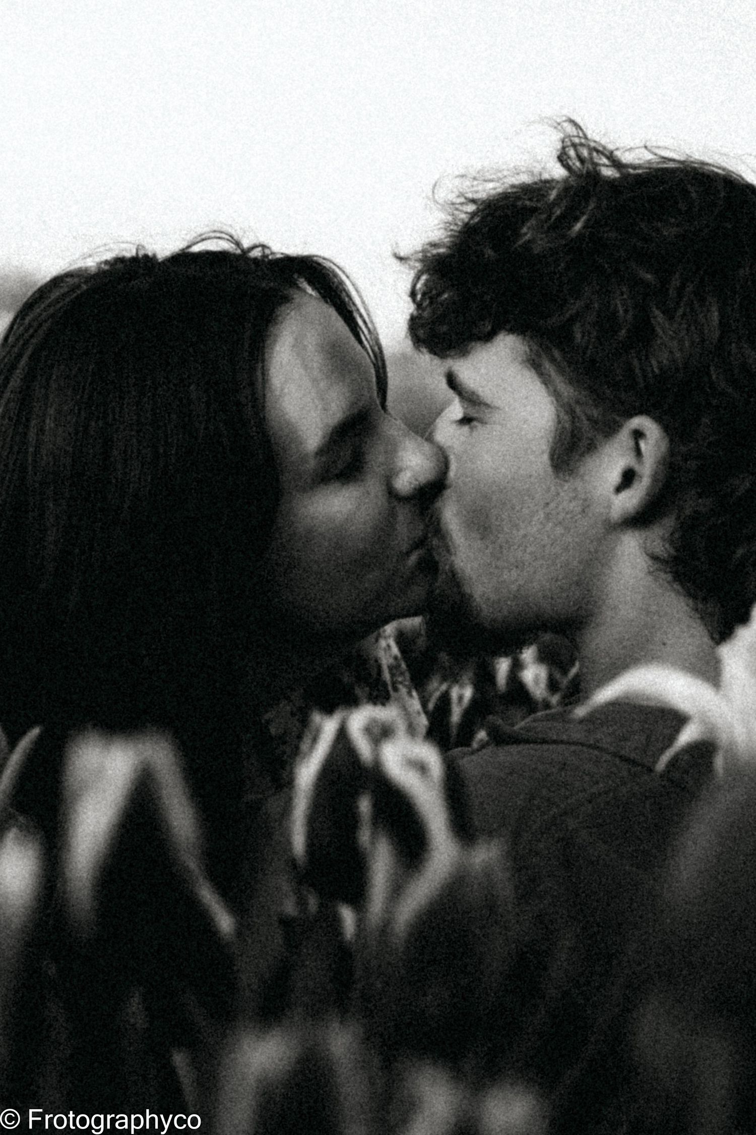 An intimate black and white close-up photograph of a couple sharing a kiss among flowers.