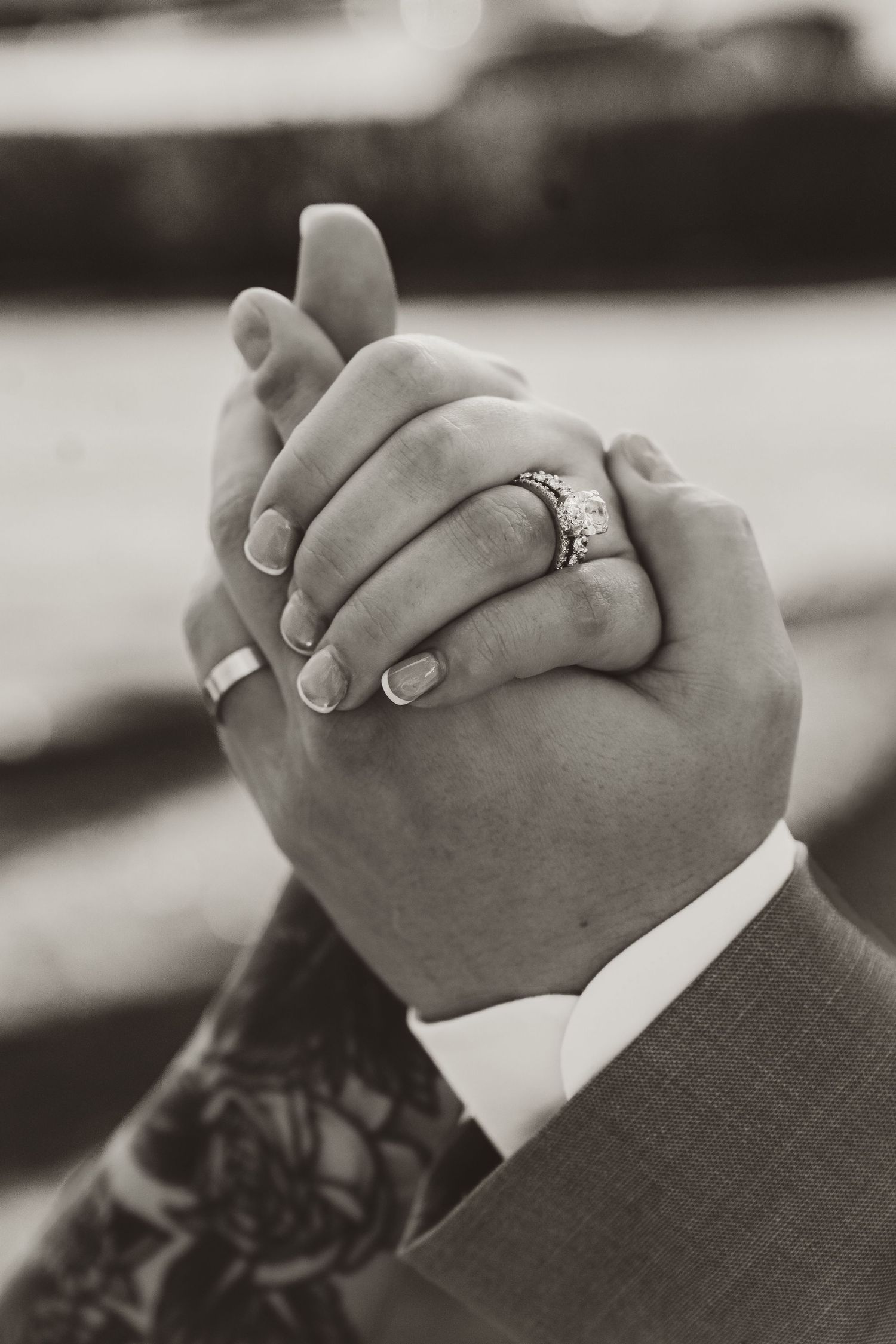 Close-up of clasped hands showing engagement ring in black and white.