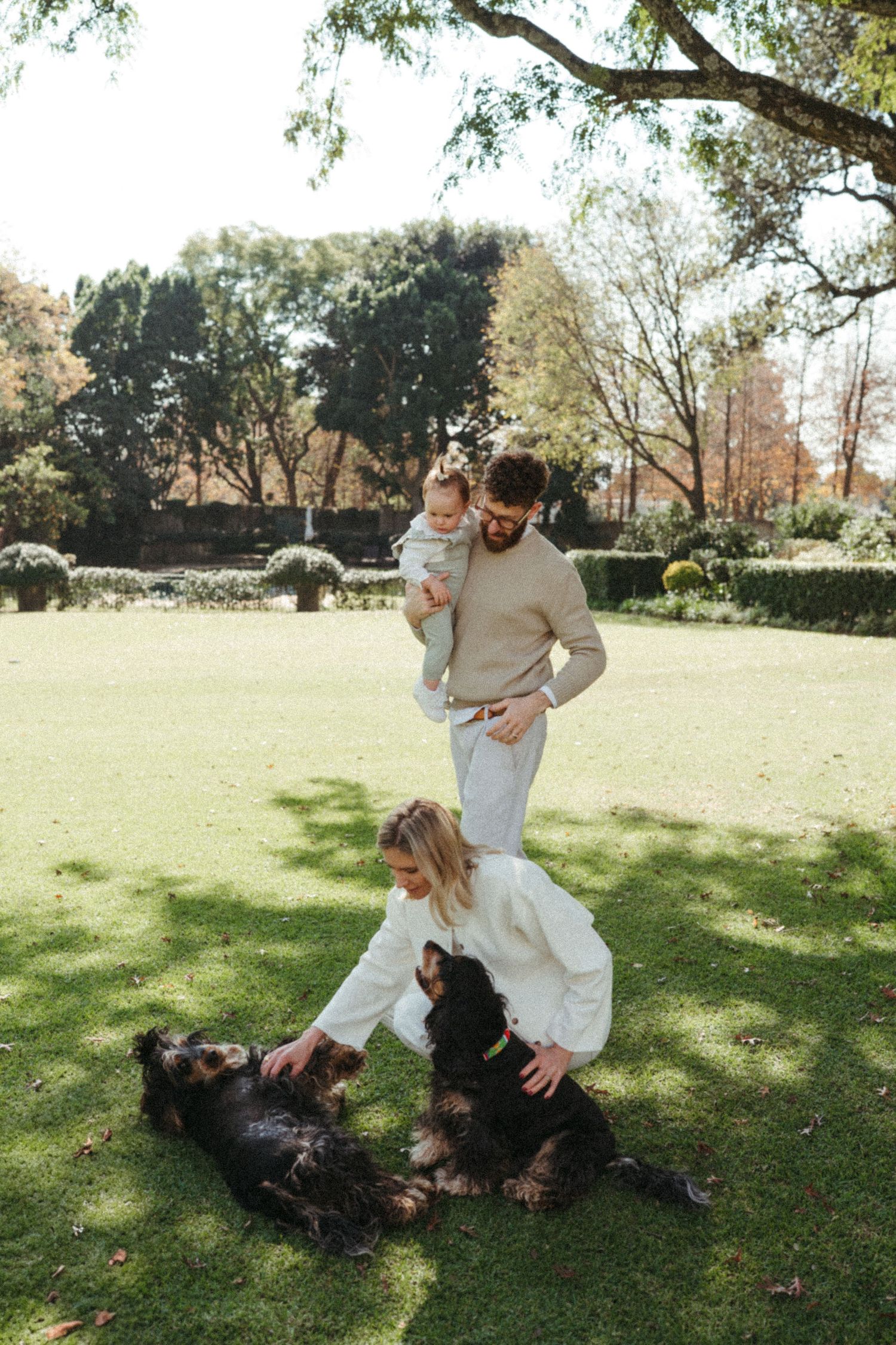 A playful scene in a grassy park with people in light colored clothing rolling and playing with a dark dog.