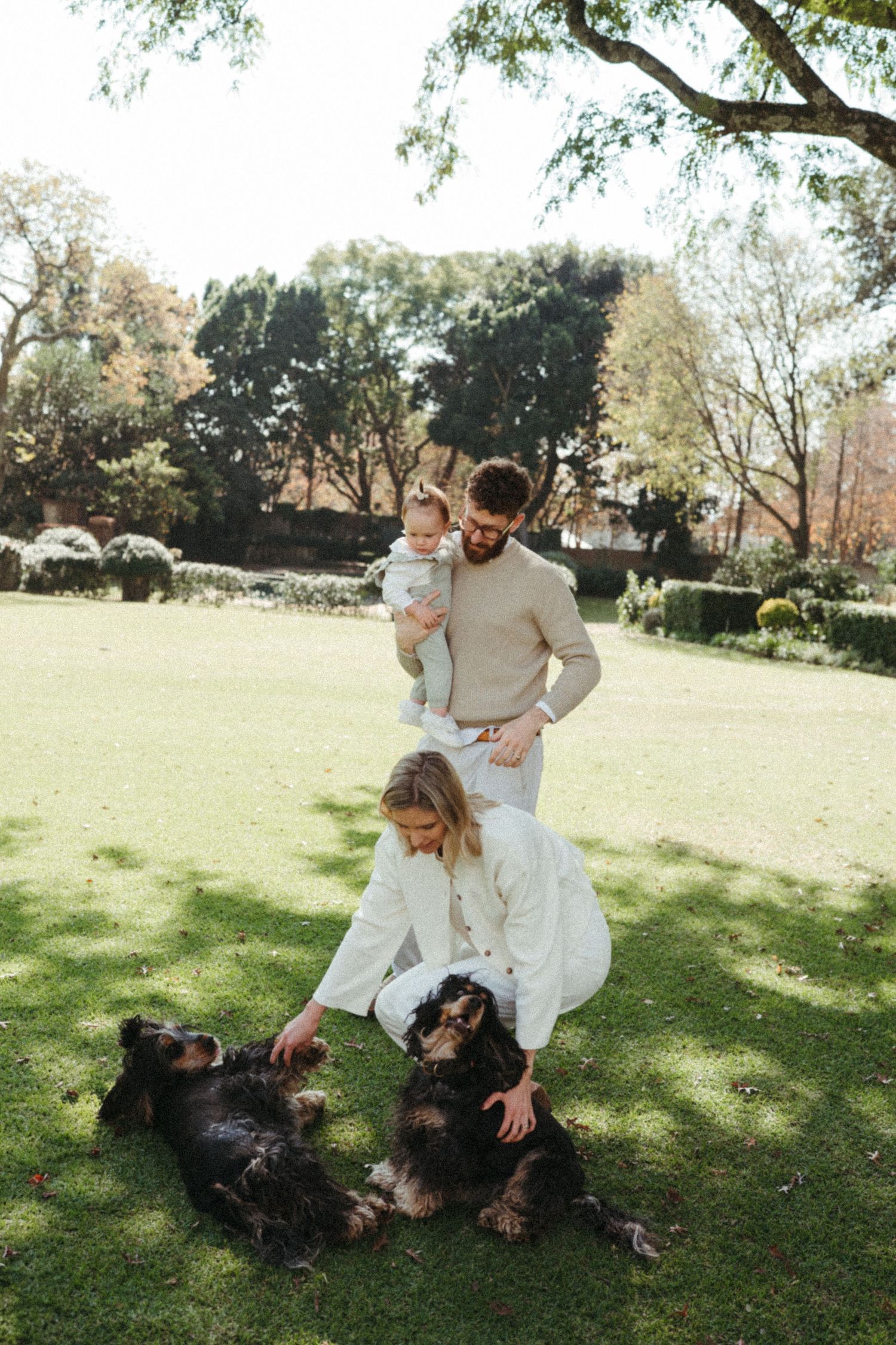 A joyful moment in a park with people in light clothing playing with a dark dog on grass.