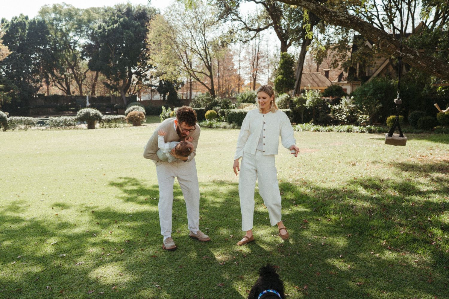 People in white outfits walking together across a sunny green lawn with trees in the background.