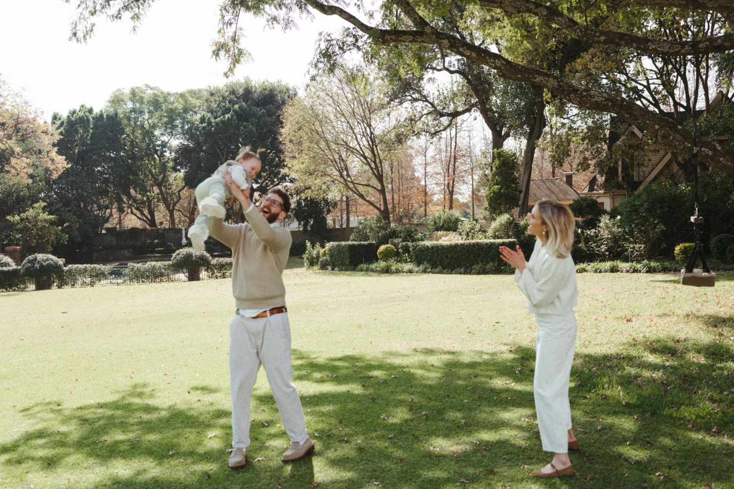 People in light colored clothing walking across a sunlit grassy field on a bright day.