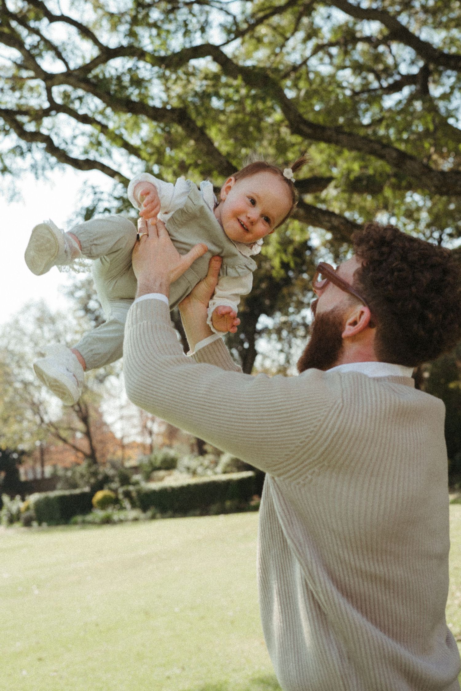 A tender family moment captured in a sunny park setting with light sweaters and natural lighting.
