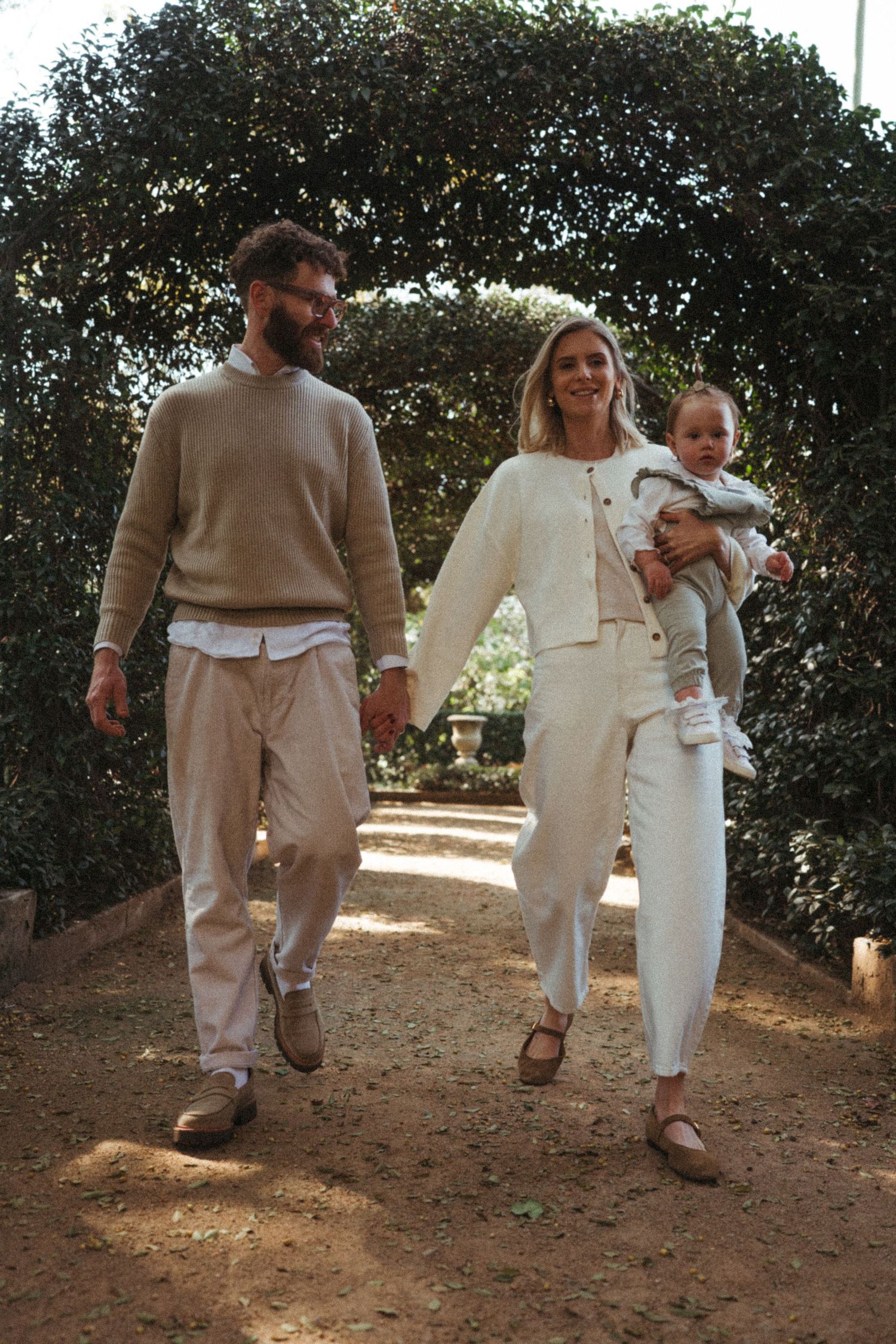 Family walking together on a dirt path wearing coordinated beige and white outfits.