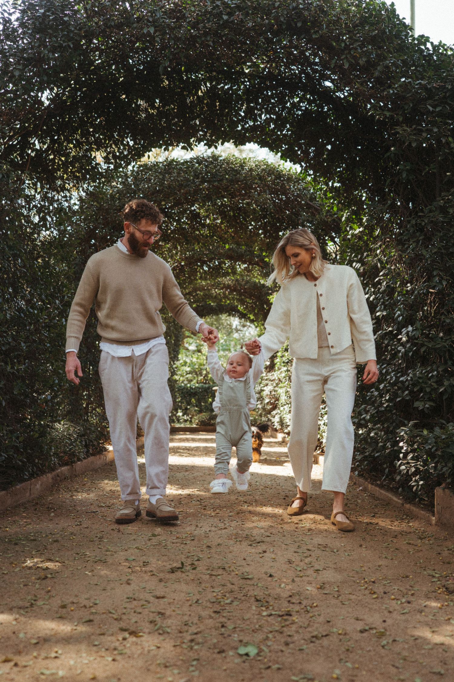 Family strolling along a shaded garden path in neutral colored clothing.