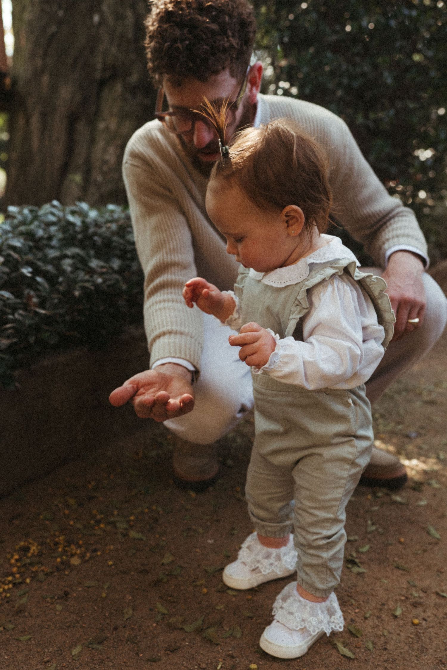 Parent helping small child take first steps on a dirt path in neutral tones.