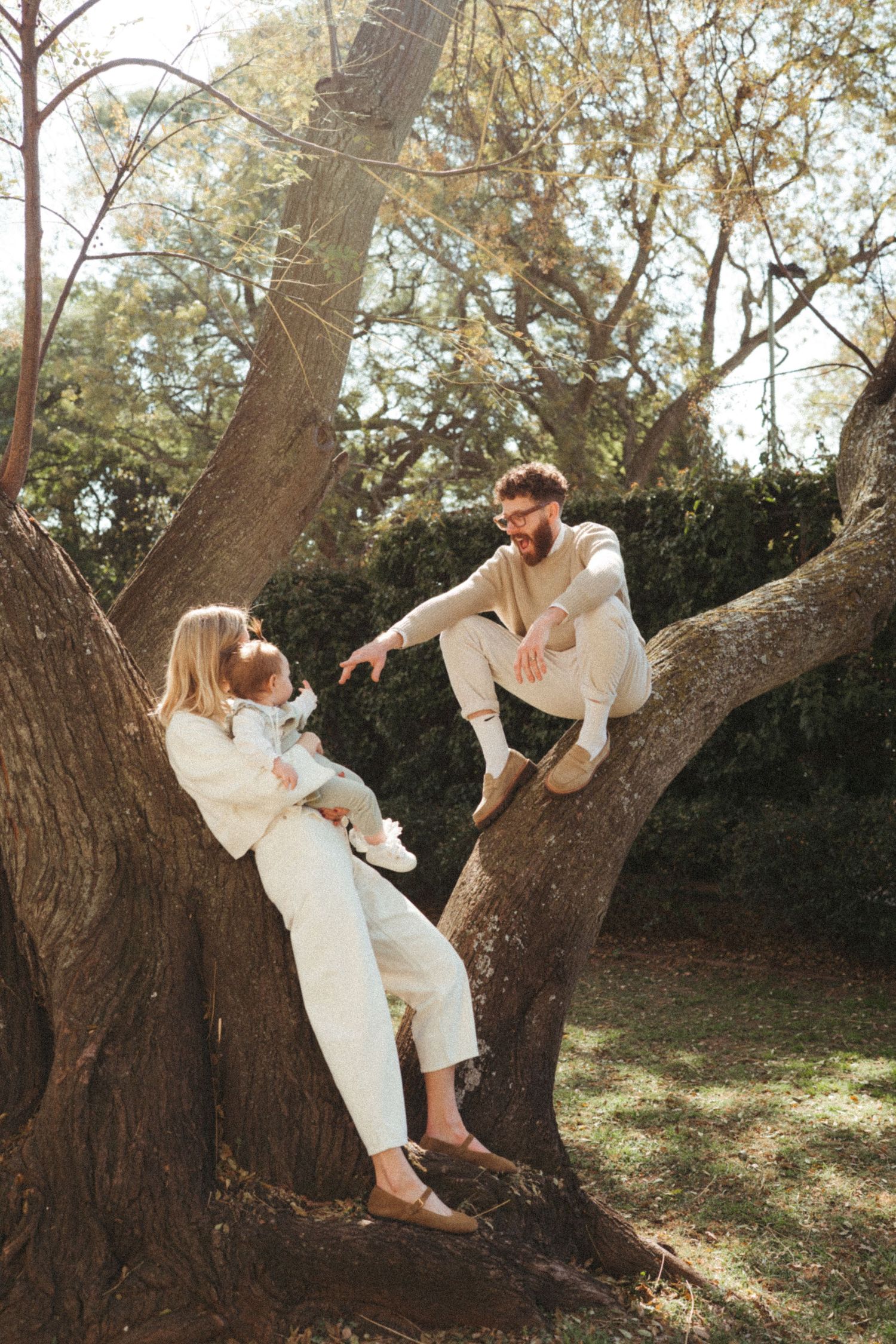 A couple in white clothing plays and poses on a large leaning tree trunk.