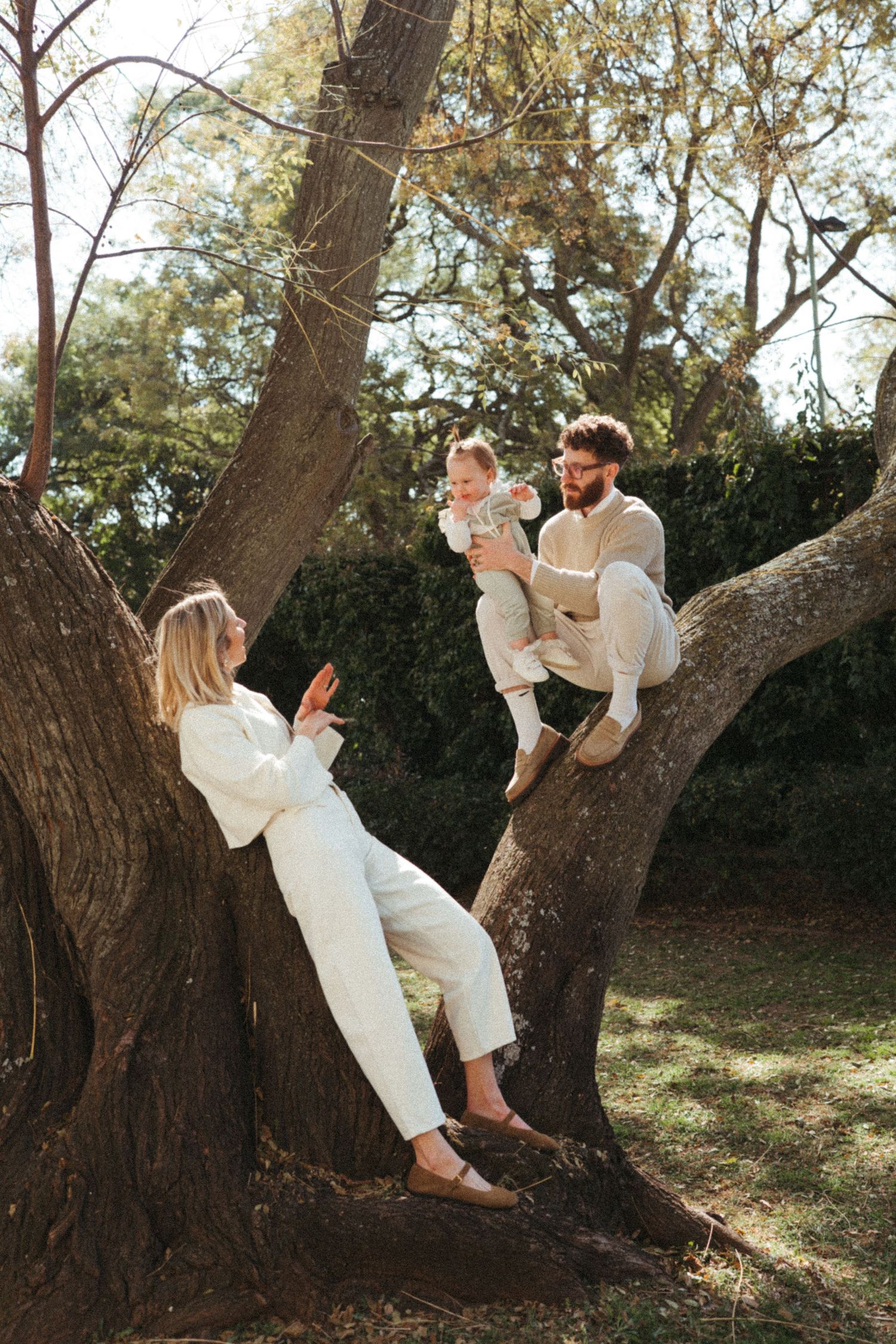 Two people in white outfits share playful moments while climbing on a large tree.