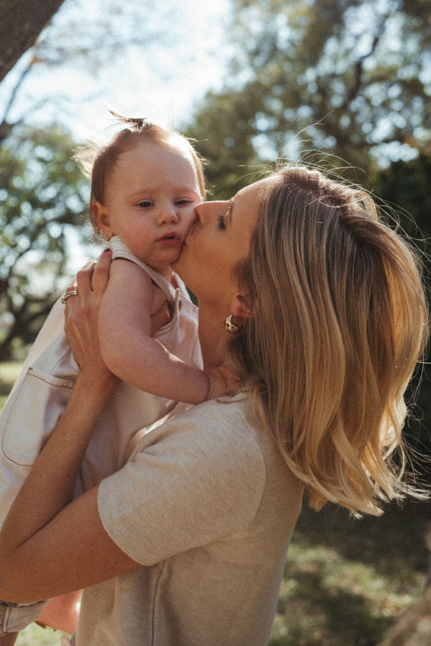A tender moment captured between parent and baby against a natural outdoor backdrop.
