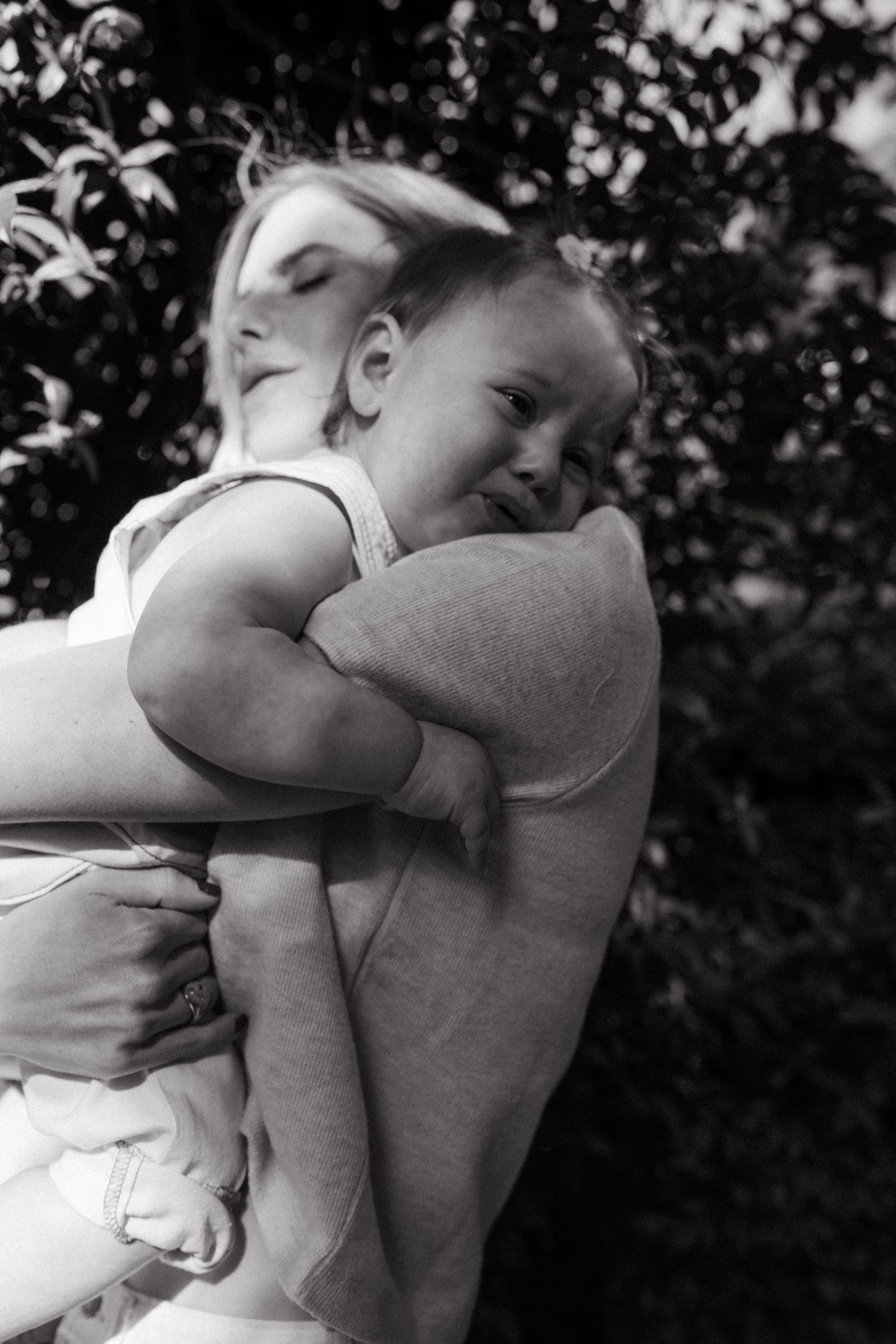 A black and white portrait captures an intimate moment between parent and child outdoors.