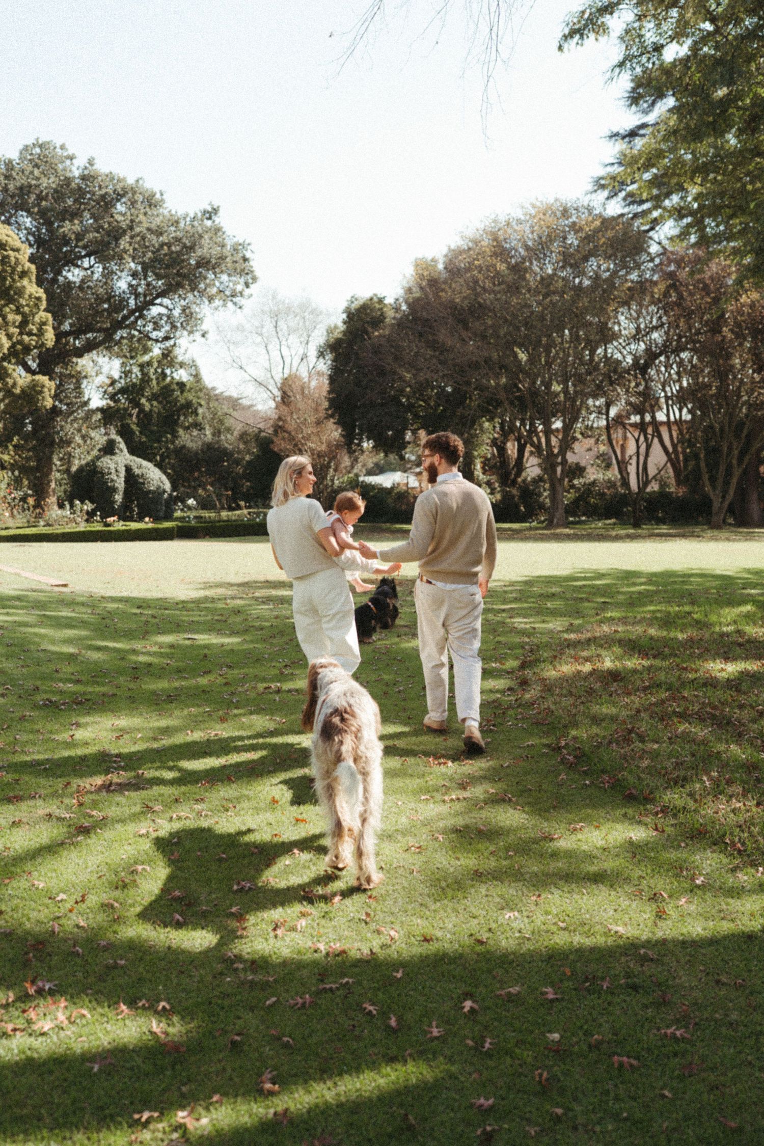 Family in white clothing walking together across a sunny grassy field.