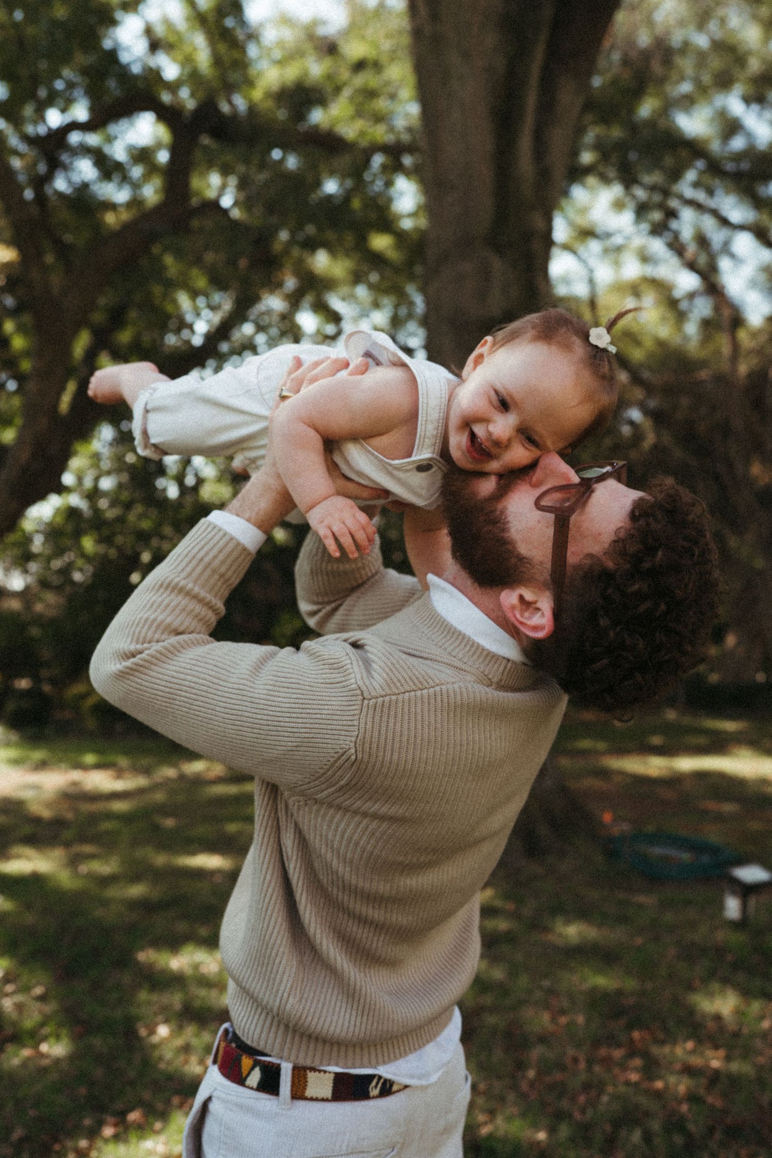 Joyful parent lifting and playing with child in a park setting.