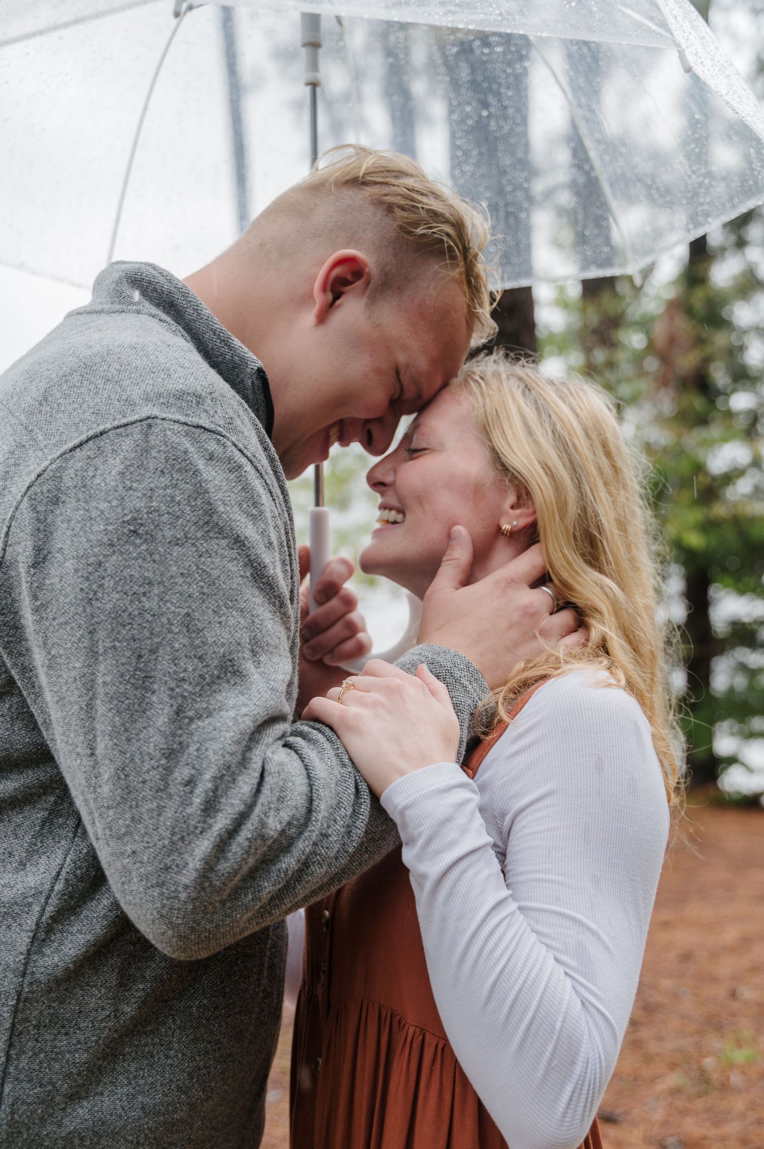 A couple embraces with joy under an umbrella on a rainy day in the woods
