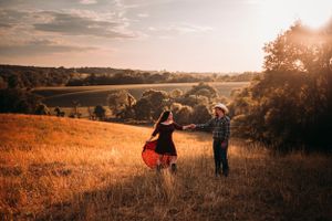 Couple dancing joyfully in a golden sunlit field, woman twirling in a red dress at sunset.