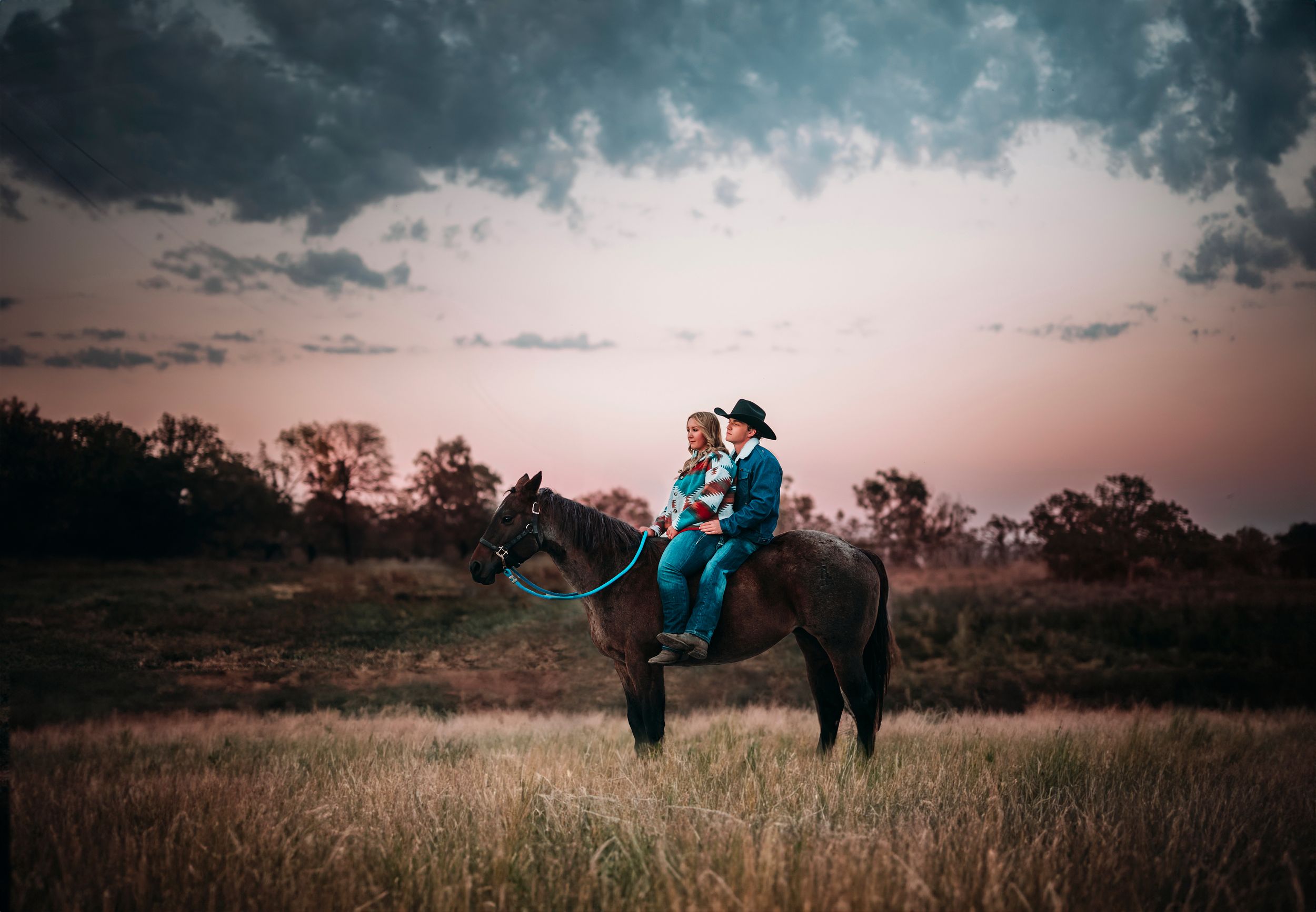 Couple riding horse together in open field during dramatic sunset.
