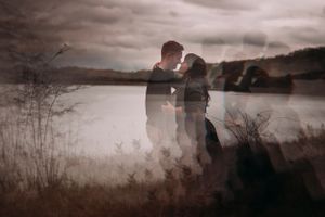 Artistic double exposure of couple kissing near lake in moody light.