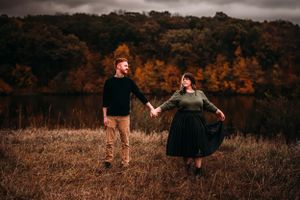 Couple holding hands walking through autumn field with colorful foliage.
