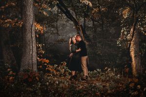 Couple kissing among autumn trees in dark moody forest setting.