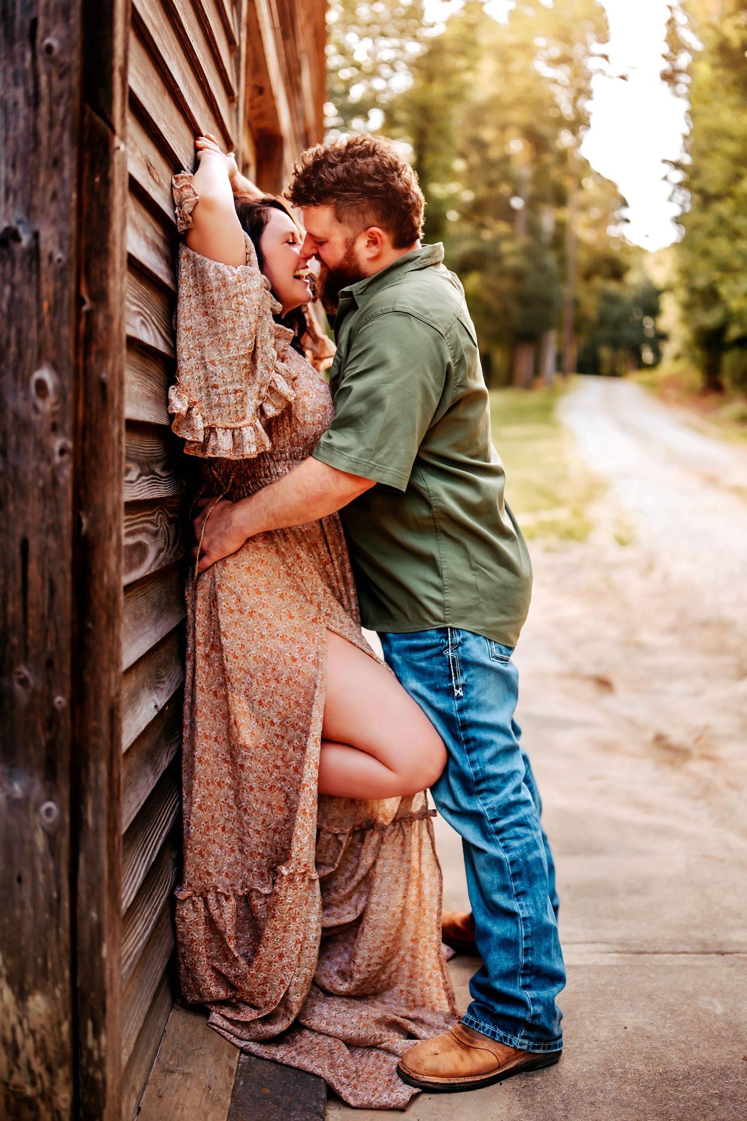 A couple shares an intimate moment outdoors, with her in a floral dress and him in denim against an urban backdrop.