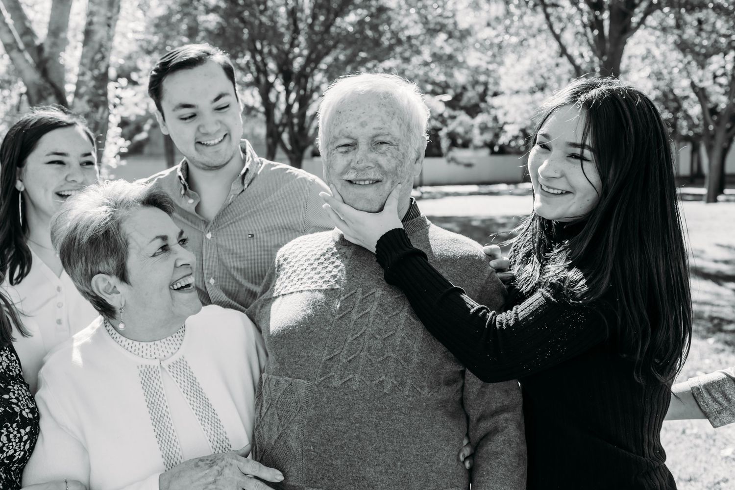 Black and white photo of a multi-generational family sharing a candid laughing moment outdoors.